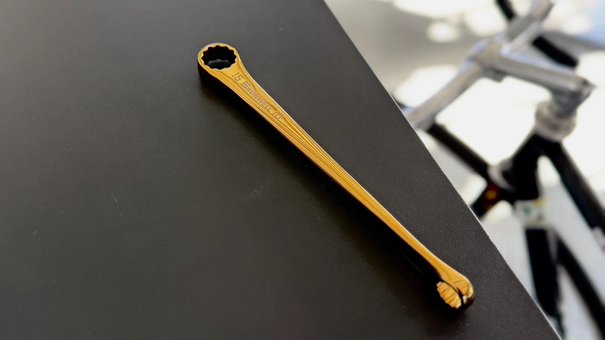 Titanium coated Gold bicycle tool by Runwell Japan, Nezile1510 15mm 10mm on a table by a NJS track fixed gear bike